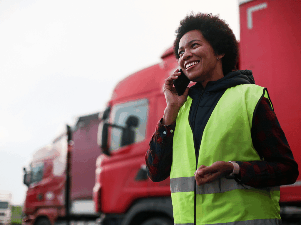 a female job seeker is making a call about hgv driving jobs. she stands in front of several parked hgvs